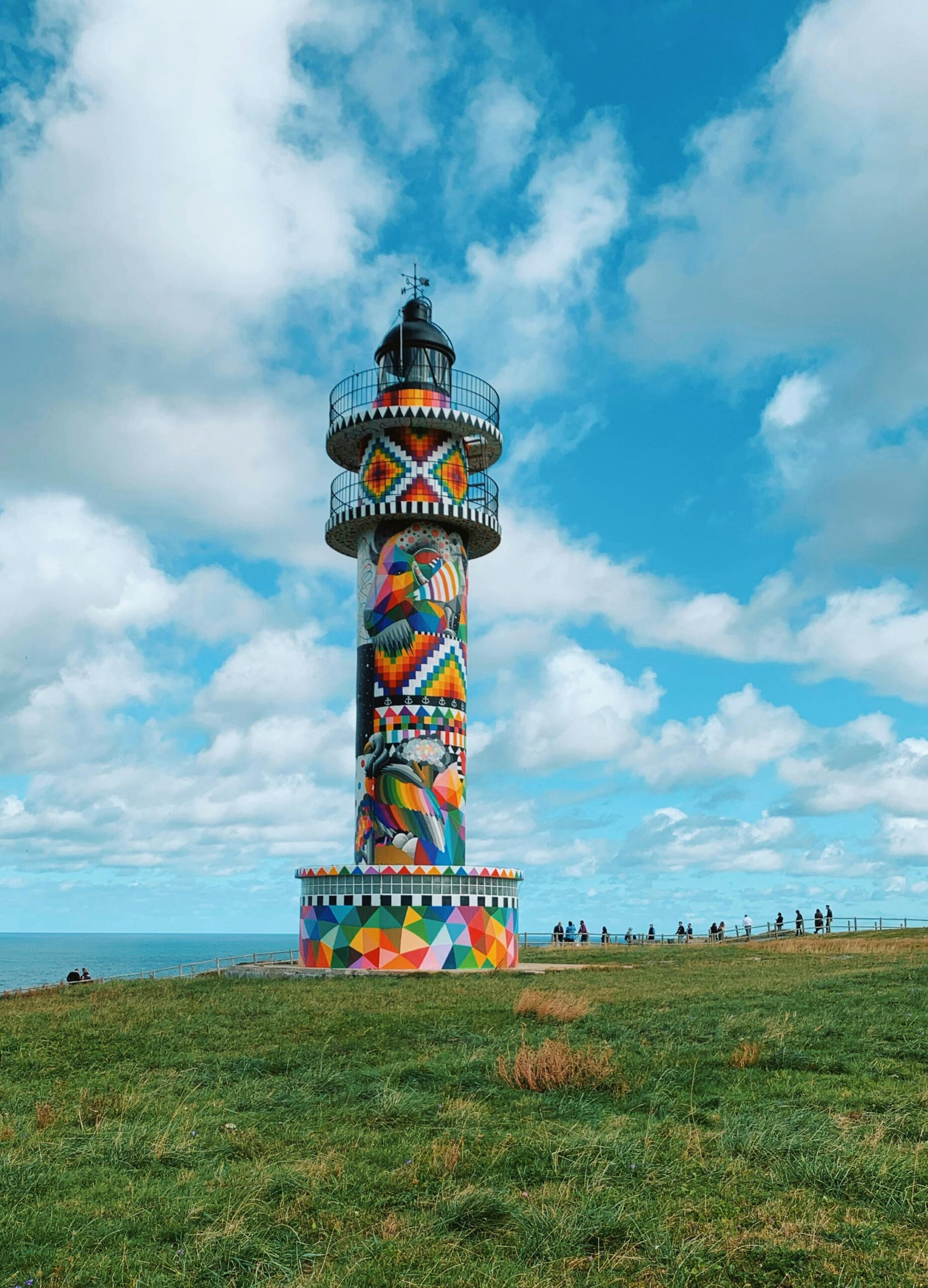 FARO AJO Vibrant painted lighthouse in Bareyo, Cantabria, under a bright blue sky with clouds.